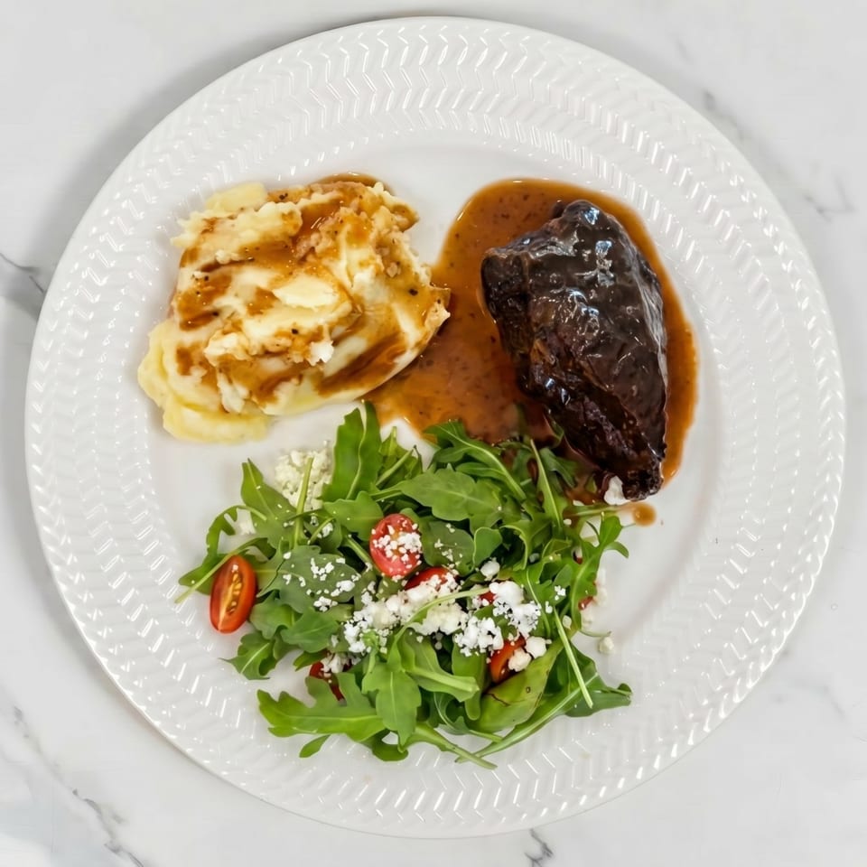 Braised short rib with mashed potatoes, gravy, and a side salad with cherry tomatoes and feta.
