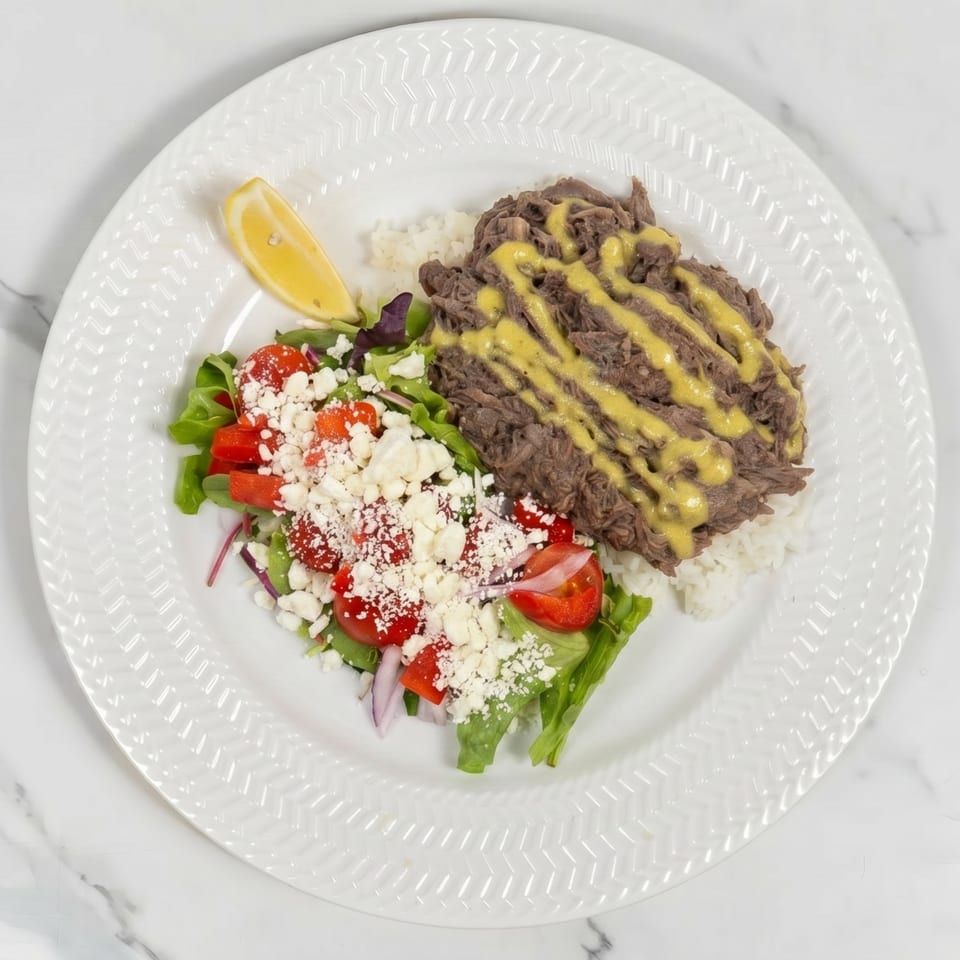 Shredded beef with yellow sauce on rice, a side salad with feta, and a lemon wedge.